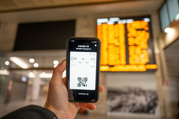 Overhead view of an human hand holding a smart phone with a digital health passport and a boarding pass from Newark (EWR) to Toronto (YYZ)
