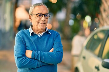 Senior grey-haired man with arms crossed smiling happy standing at the city.