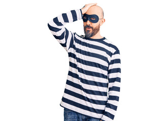 Young handsome man wearing burglar mask surprised with hand on head for mistake, remember error....