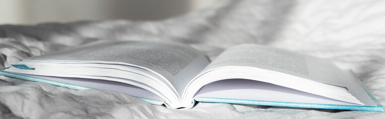 Banner of opened book on grey crumpled sheet with sunshine light. Home hobby concept 
