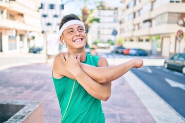 Young hispanic sportsman using earphones stretching at street of city