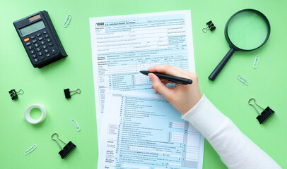 The person writes on the 1040 tax form. There are a lot of stationery and a calculator on the table. 1040 Individual Income Tax Return 