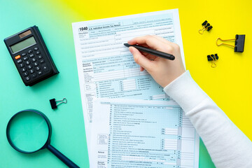 Hand fills out 1040 tax form on a bright green-yellow background. US Taxation Concept 