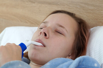 teenage girl breathing through an inhaler while lying in bed, asthma attack or bronchitis