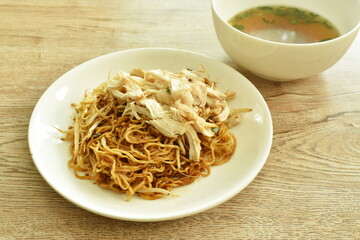 dry chinese yellow egg noodles dressing sweet black soy sauce  topping slice boiled chicken on plate and soup bowl