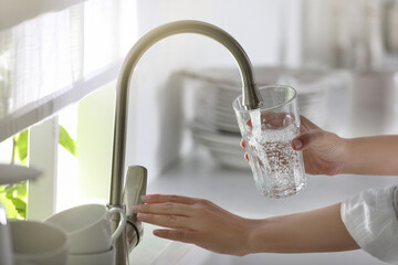 Woman pouring water into glass in kitchen, closeup