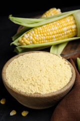 Fototapeta na wymiar Corn flour in bowl and fresh cobs on black table