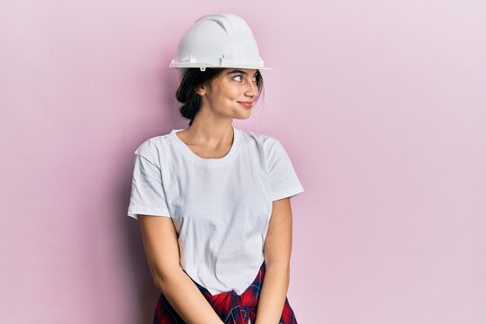 Young caucasian woman wearing hardhat smiling looking to the side and staring away thinking.