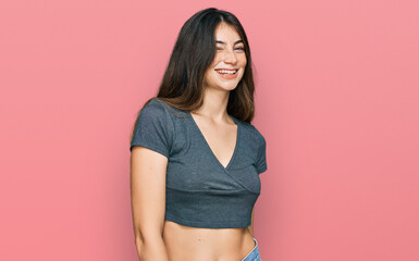 Young beautiful teen girl wearing casual crop top t shirt winking looking at the camera with sexy...