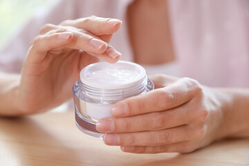 Woman with jar of moisturizing cream at table, closeup