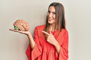 Young beautiful woman holding brain smiling happy pointing with hand and finger