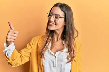 Young beautiful woman wearing business style and glasses looking proud, smiling doing thumbs up gesture to the side