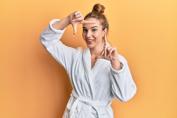 Young blonde woman wearing bathrobe smiling making frame with hands and fingers with happy face. creativity and photography concept.