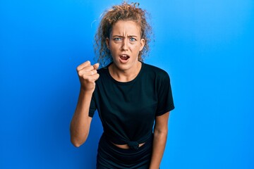 Naklejka premium Beautiful caucasian teenager girl wearing black sportswear angry and mad raising fist frustrated and furious while shouting with anger. rage and aggressive concept.
