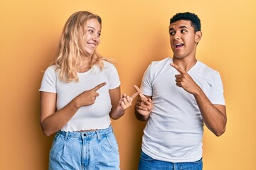 Young interracial couple wearing casual white tshirt smiling and looking at the camera pointing with two hands and fingers to the side.