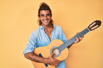 Young hispanic man playing classical guitar smiling with a happy and cool smile on face. showing teeth.