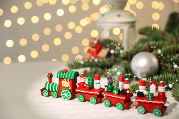 Toy train and Christmas decor on white table against blurred lights