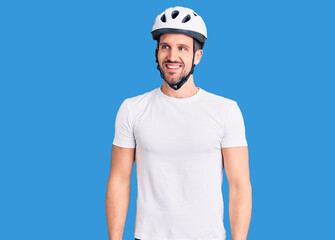 Young handsome man wearing bike helmet looking away to side with smile on face, natural expression. laughing confident.
