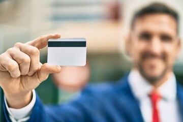 Young caucasian businessman smiling happy holding credit card at the city.