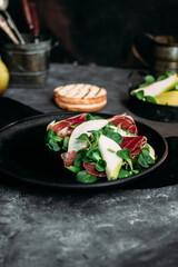 Parma, pear and spinach salad on black plate