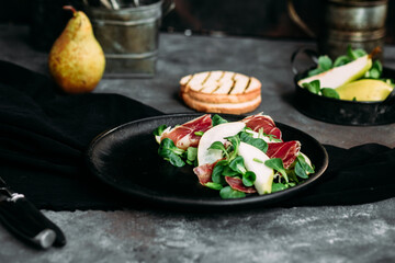Parma, pear and spinach salad on black plate