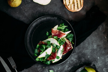 Parma, pear and spinach salad on black plate