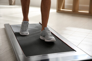 Sporty man training on walking treadmill at home, closeup