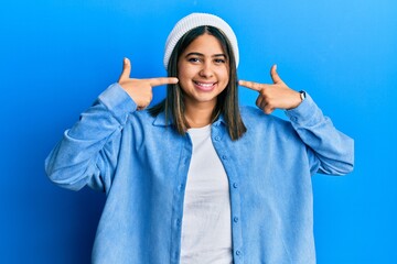 Young latin woman wearing cute wool cap smiling cheerful showing and pointing with fingers teeth and mouth. dental health concept.