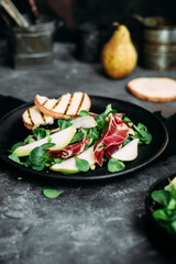 Parma, pear and spinach salad on black plate