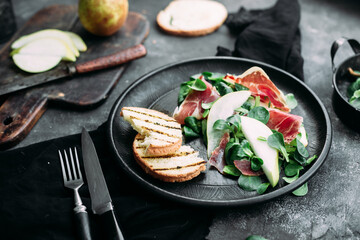 Parma, pear and spinach salad on black plate
