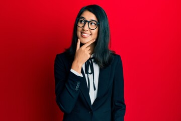 Beautiful asian young woman wearing business suit with hand on chin thinking about question, pensive expression. smiling with thoughtful face. doubt concept.