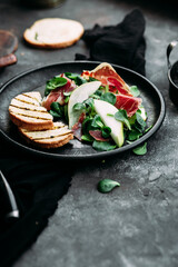 Parma, pear and spinach salad on black plate
