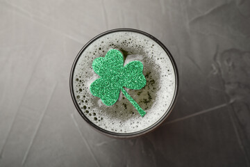 Glass of beer with clover leaf on grey table, top view. St Patrick's Day celebration
