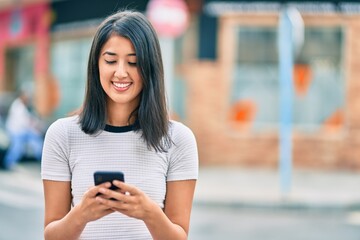 Young hispanic woman smiling happy using smartphone at the city.