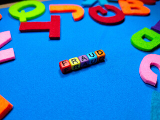 Selective focus.Colorful dice with word FRAUD on blue background.Shot were noise and film grain.