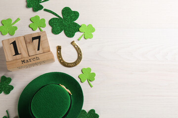Flat lay composition with leprechaun hat and block calendar on white wooden table, space for text....
