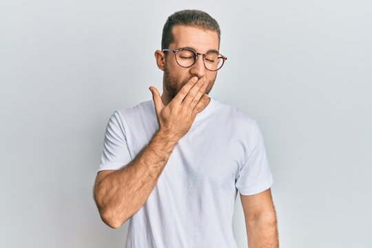 Young caucasian man wearing casual clothes and glasses bored yawning tired covering mouth with hand. restless and sleepiness.