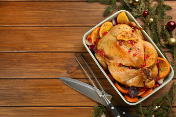 Roasted chicken with oranges, pomegranate and vegetables near fir tree branches on wooden table, flat lay. Space for text