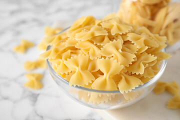 Raw pasta in bowl on white marble table, closeup