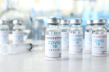 Glass vials with COVID-19 vaccine on white wooden table