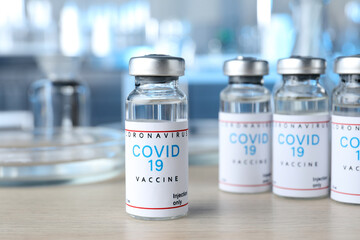 Glass vials with COVID-19 vaccine on wooden table