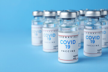 Vials with coronavirus vaccine on light blue background, space for text