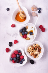 heart-shaped white ceramic bowls arranged on a lightly textured background with berries, dried fruit, plain yogurt, wholemeal flakes and honey