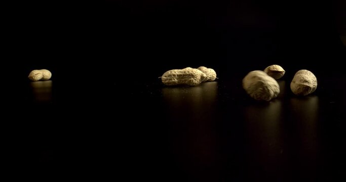 Appetizing peanuts falling on a black surface. Fresh peanuts isolated on black background in light studio light. High quality.