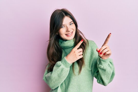 Young beautiful caucasian girl wearing wool sweater smiling and looking at the camera pointing with two hands and fingers to the side.