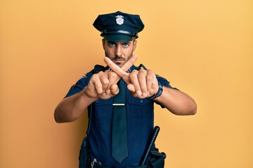 Handsome hispanic man wearing police uniform rejection expression crossing fingers doing negative...