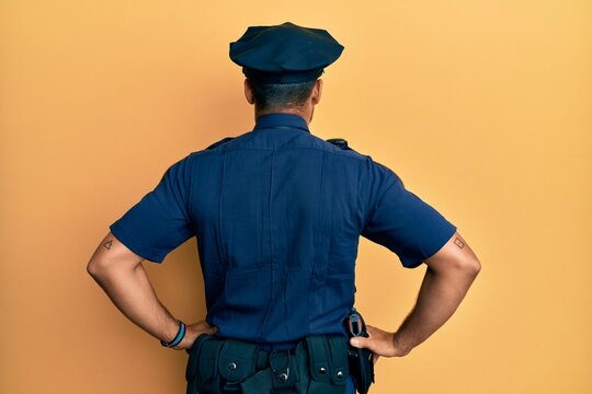 Handsome hispanic man wearing police uniform standing backwards looking away with arms on body