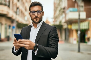 Young hispanic businessman with serious expression using smartphone at the city.