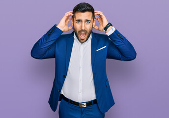 Fototapeta premium Young hispanic man wearing business jacket crazy and scared with hands on head, afraid and surprised of shock with open mouth