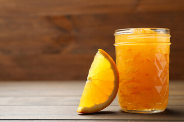 Delicious orange marmalade and citrus fruit slice on wooden table, closeup. Space for text